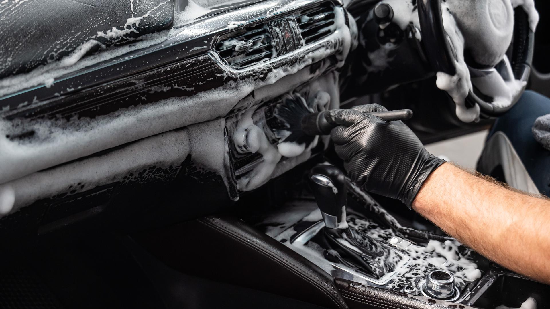 A mechanic cleans the interior of a car with a brush and foam.