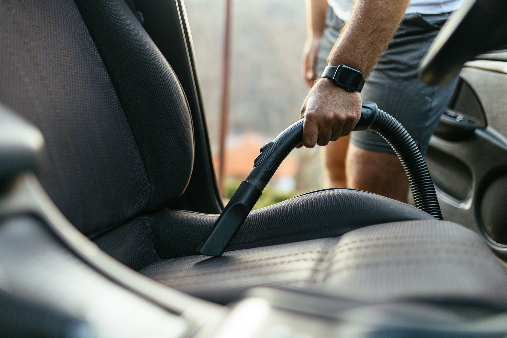 Man Vacuuming Car Seat Interior with Vacuum Cleaner in Sunlight